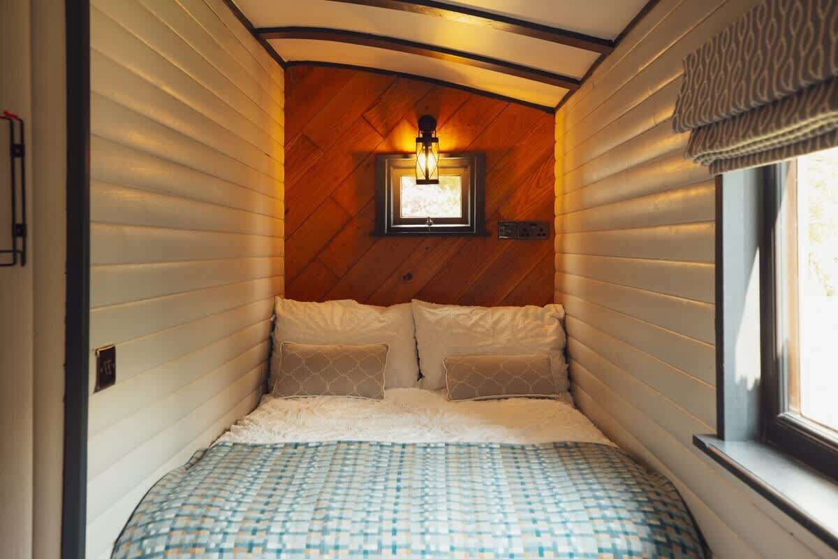A cozy bedroom with a wooden ceiling, a bed with patterned bedding, and a window with curtains.