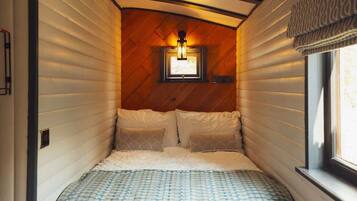 A cozy bedroom with a wooden ceiling, a bed with patterned bedding, and a window with curtains.
