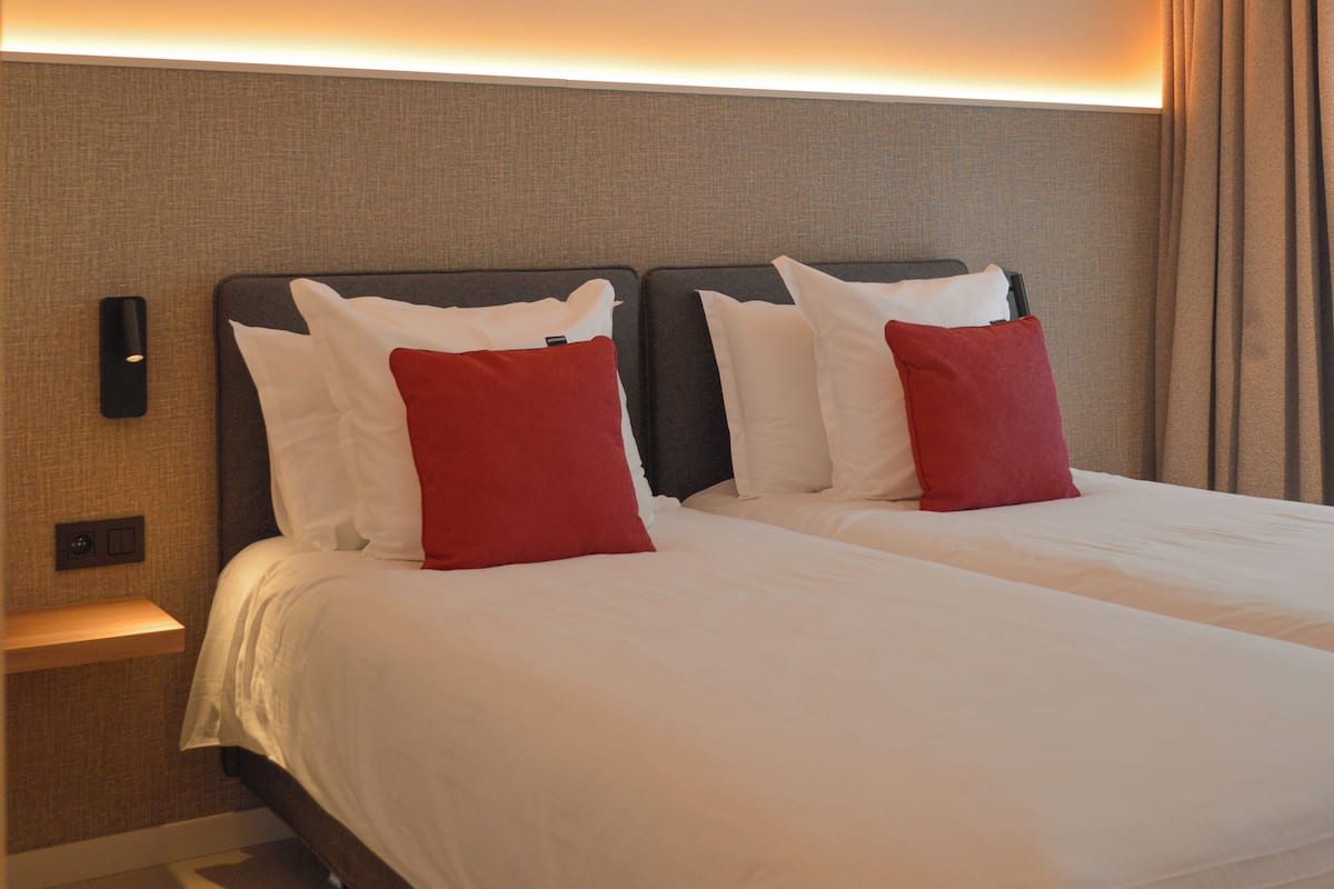 A hotel room with a large bed, two nightstands, and a wall-mounted light fixture.