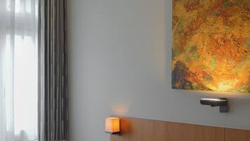 Een hotelkamer met een bed, een nachtkastje, een wandlamp, een raam met gordijnen en een schilderij aan de muur.