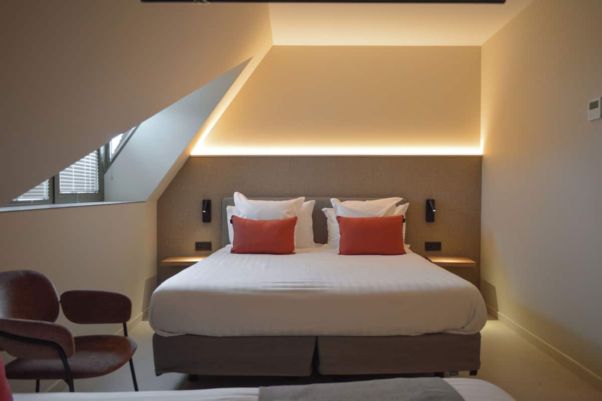 A modern bedroom with a large bed, two nightstands, a chair, and a sloped ceiling with skylight.