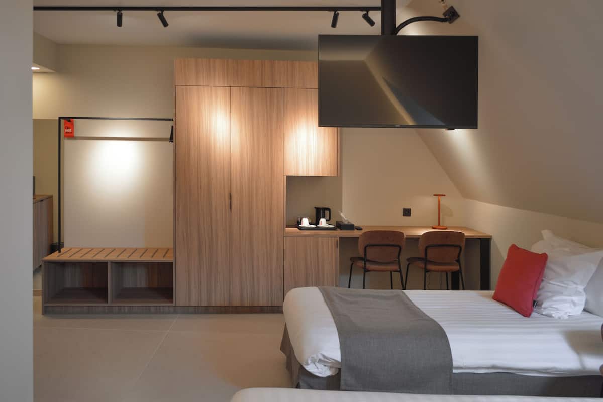 A modern hotel room with a bed, a desk, and a kitchenette area.