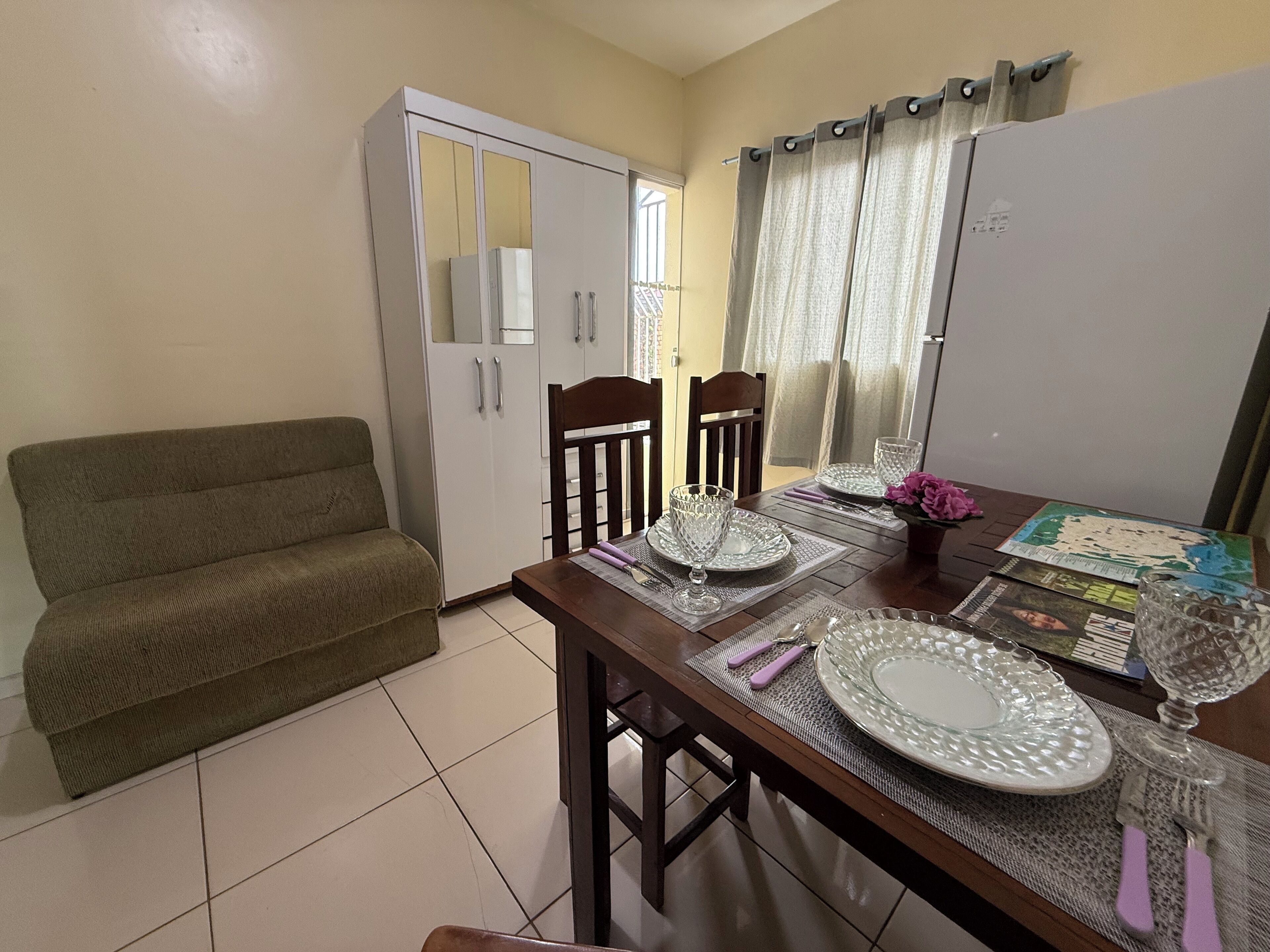 A dining area with a wooden table set for four, a sofa, and a white wardrobe.