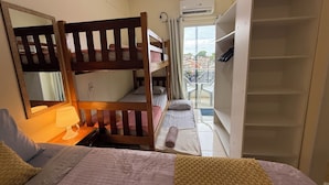 Une chambre de dortoir avec des lits superposés, un miroir, une lampe, une armoire et une fenêtre donnant sur la ville.
