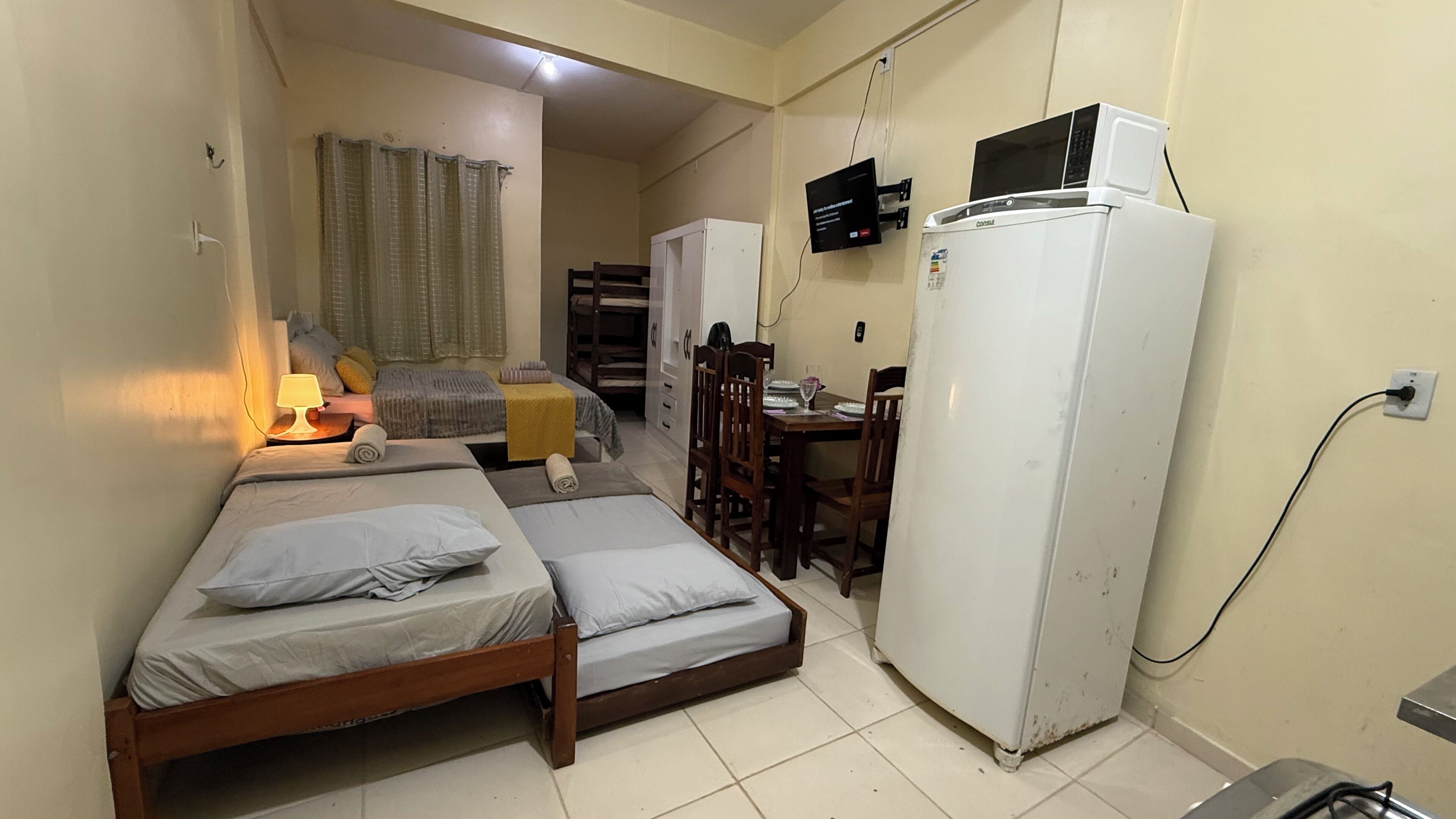 A small, compact room with a bed, a desk, a chair, a refrigerator, and a television.