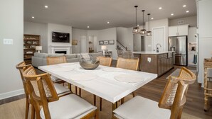 A modern kitchen with a central island, built-in appliances, and a dining area with a white table and wooden chairs. - 15325 West Kea Way, Tower Hill: 4  BR, 3.5  BA House in Lewes, Sleeps 8 (Lewes)