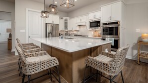 A modern kitchen with a large island, stainless steel appliances, and wicker bar stools. - 15325 West Kea Way, Tower Hill: 4  BR, 3.5  BA House in Lewes, Sleeps 8 (Lewes)