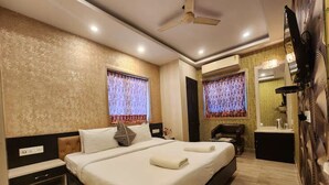 A hotel room with a large bed, a desk, a chair, a TV, and an air conditioning unit. - Hotel Orchid Plaza (Kolkata)