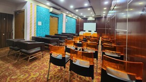 A conference room with rows of chairs, a projector screen, and a patterned carpet. - Hotel Orchid Plaza (Kolkata)
