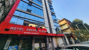 A multi-story hotel with a red and blue facade, featuring a sign for 'Hotel Orchid Plaza' and 'Rooms & Banquet'. - Hotel Orchid Plaza (Kolkata)