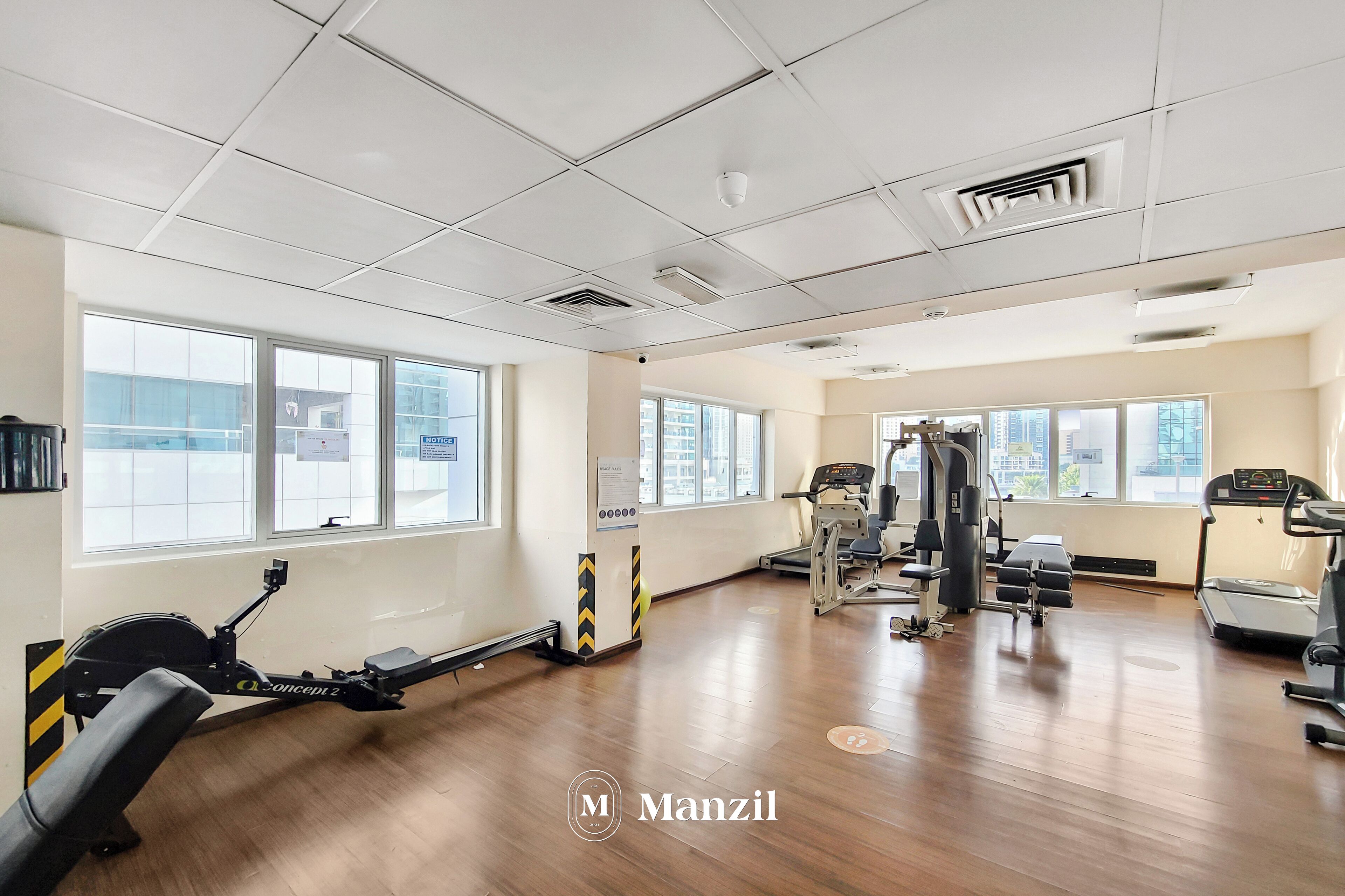 Un gimnasio amplio con máquinas de cardio, pesas y grandes ventanales que ofrecen vistas de la ciudad.