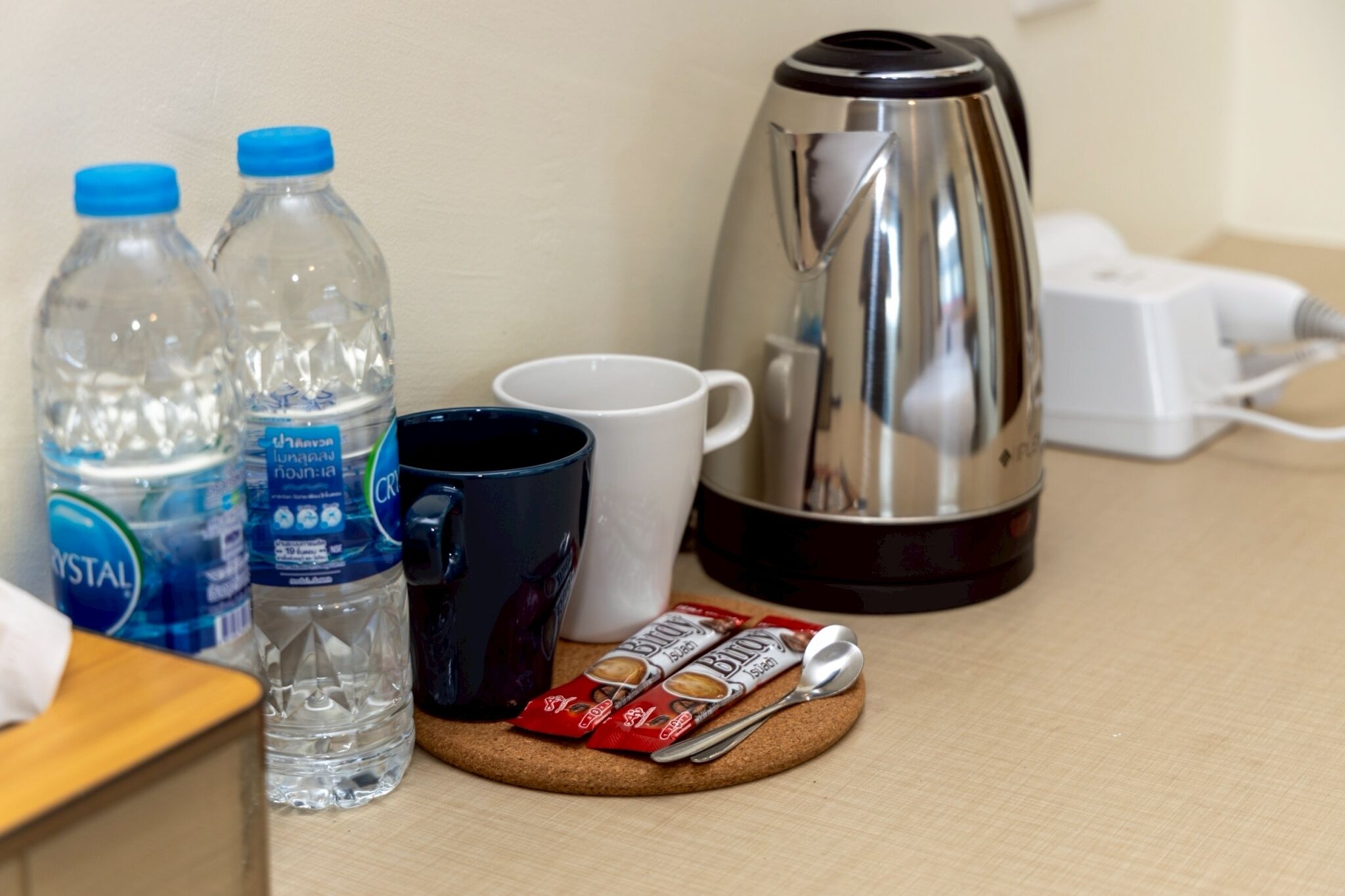 Ein Tisch mit zwei Wasserflaschen, einer Kaffeekanne, einer Tasse, einer Snackpackung und einem Löffel.