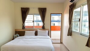 A hotel room with a large bed, a nightstand, a window with curtains, and a view of buildings outside. - Sea Inn Pattaya (Pattaya)