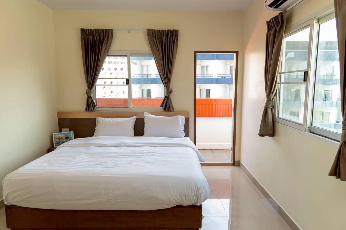 A hotel room with a large bed, a nightstand, a window with curtains, and a view of buildings outside.