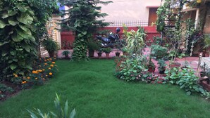 Ein gepflegter Garten mit verschiedenen Pflanzen und Blumen, einem ordentlich gestutzten Rasen und einem abgestellten Motorrad.