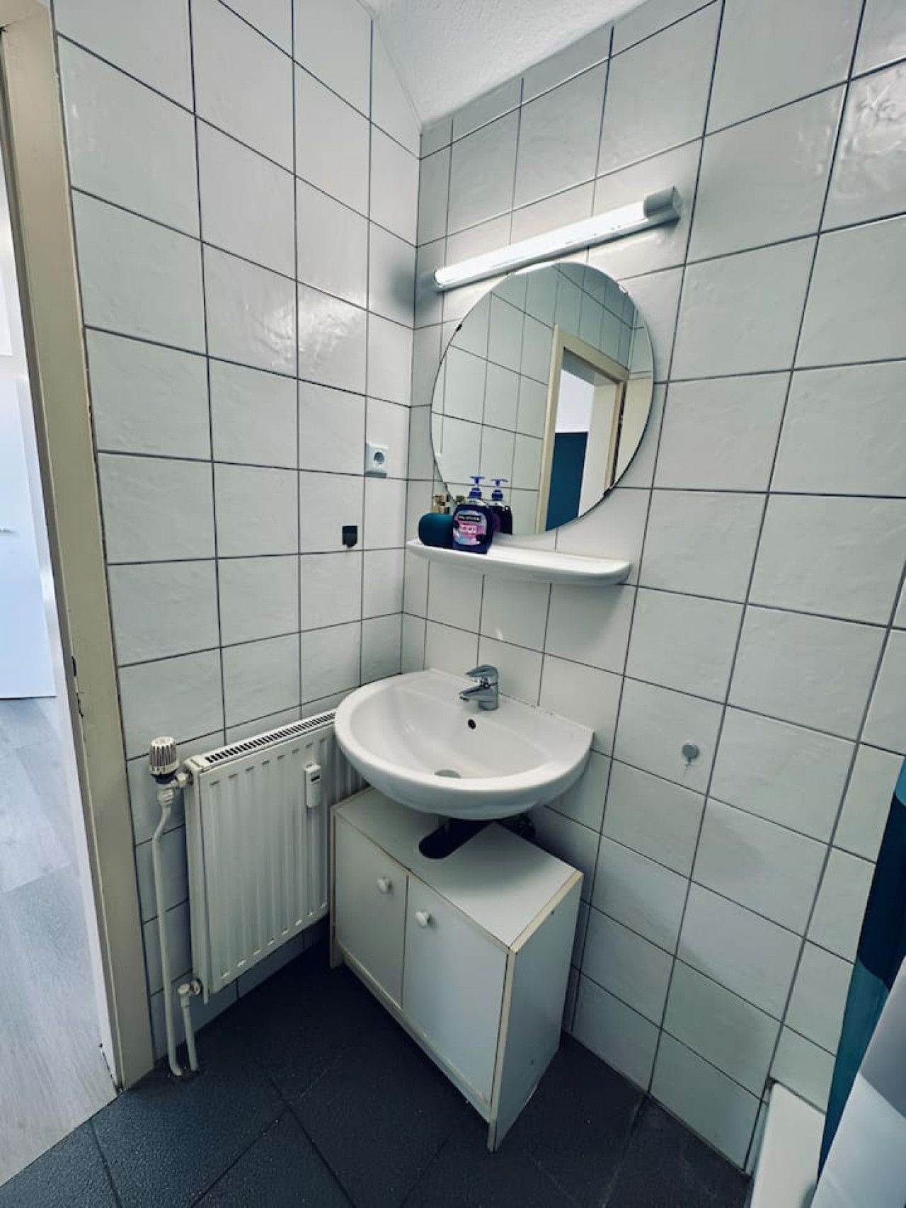 Een kleine, compacte badkamer met witte tegels, een wit wastafel, een spiegel en een radiator.