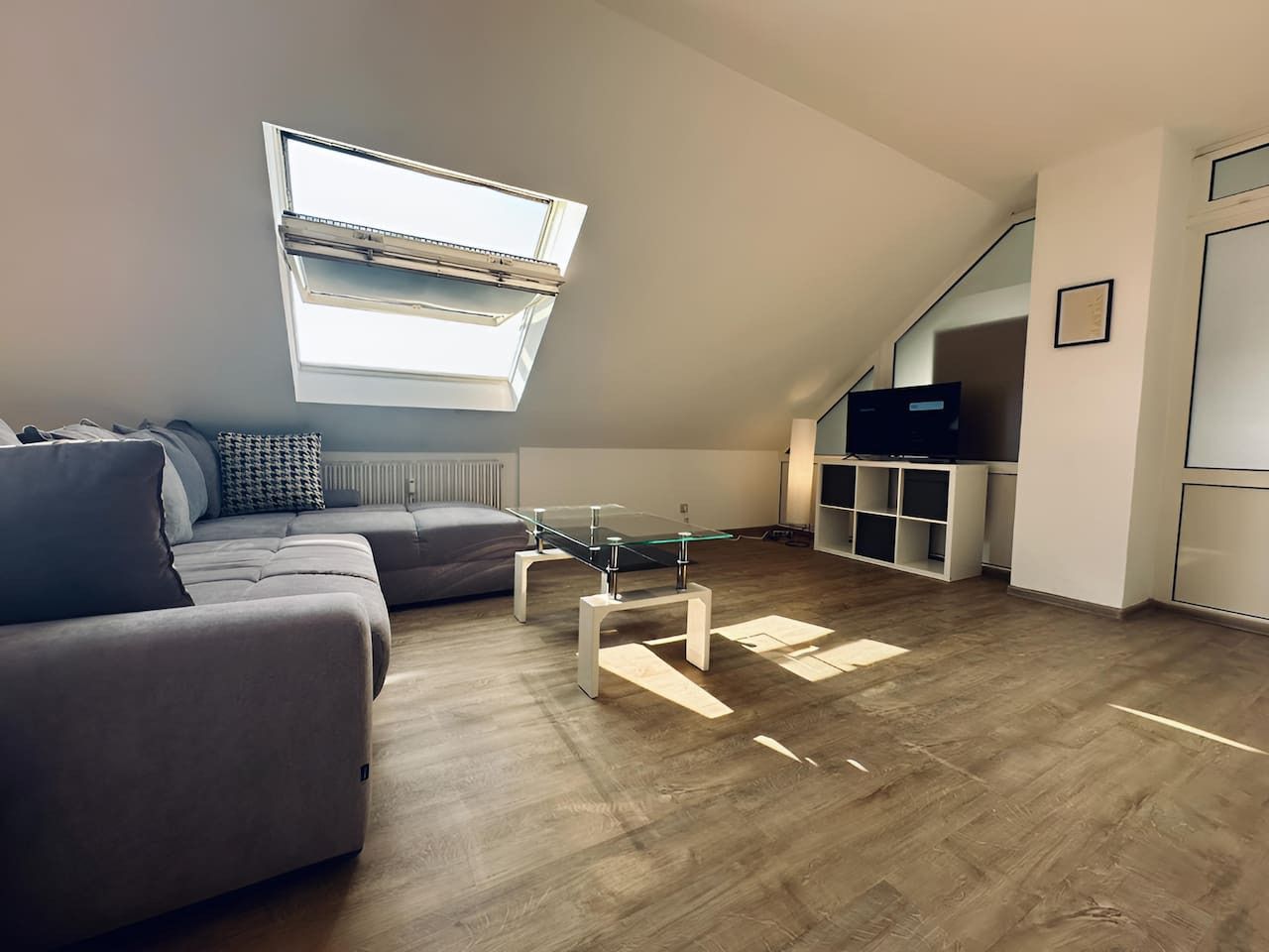 A modern living room with a glass-top coffee table, grey sofa, and a built-in TV shelf.
