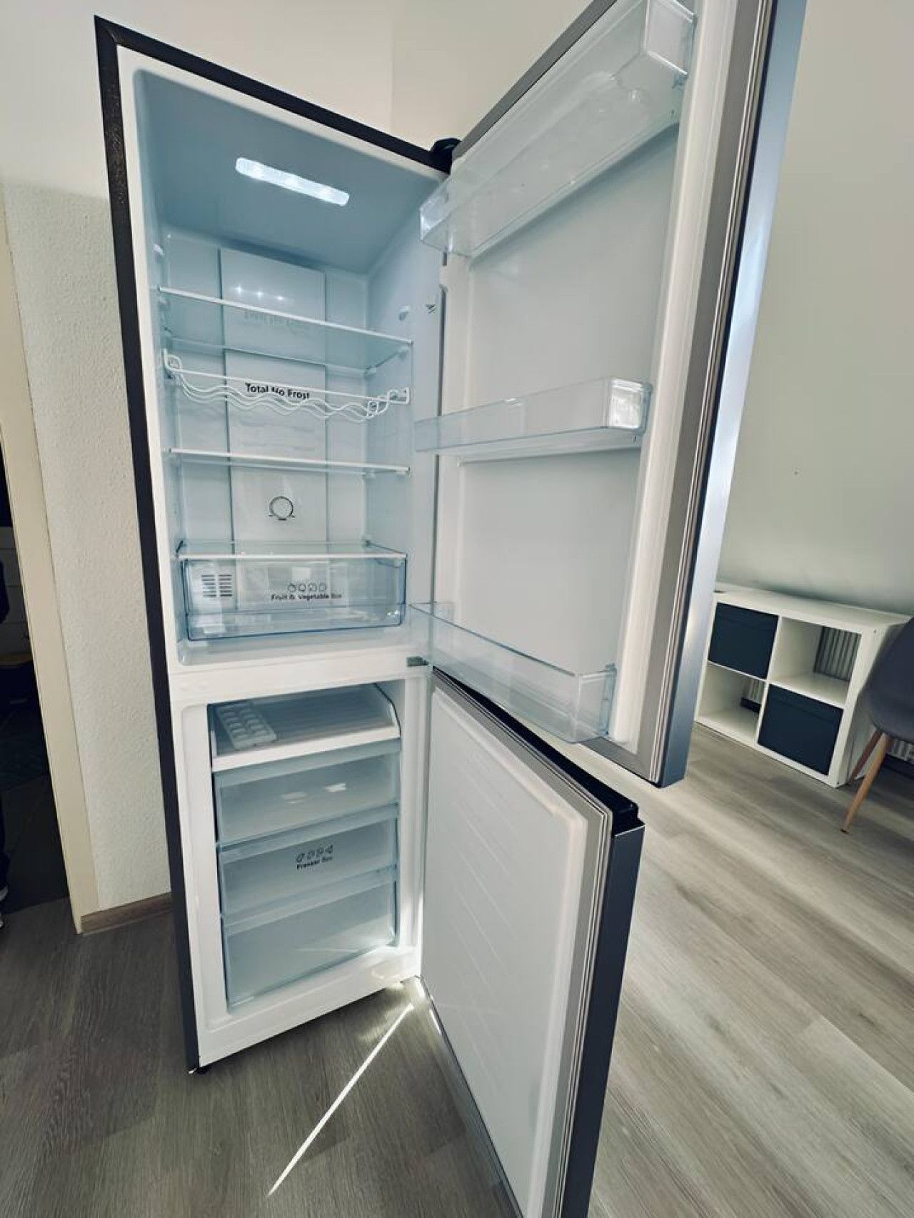 Un refrigerador abierto con varios estantes y cajones, un dispensador de agua y un compartimento congelador.