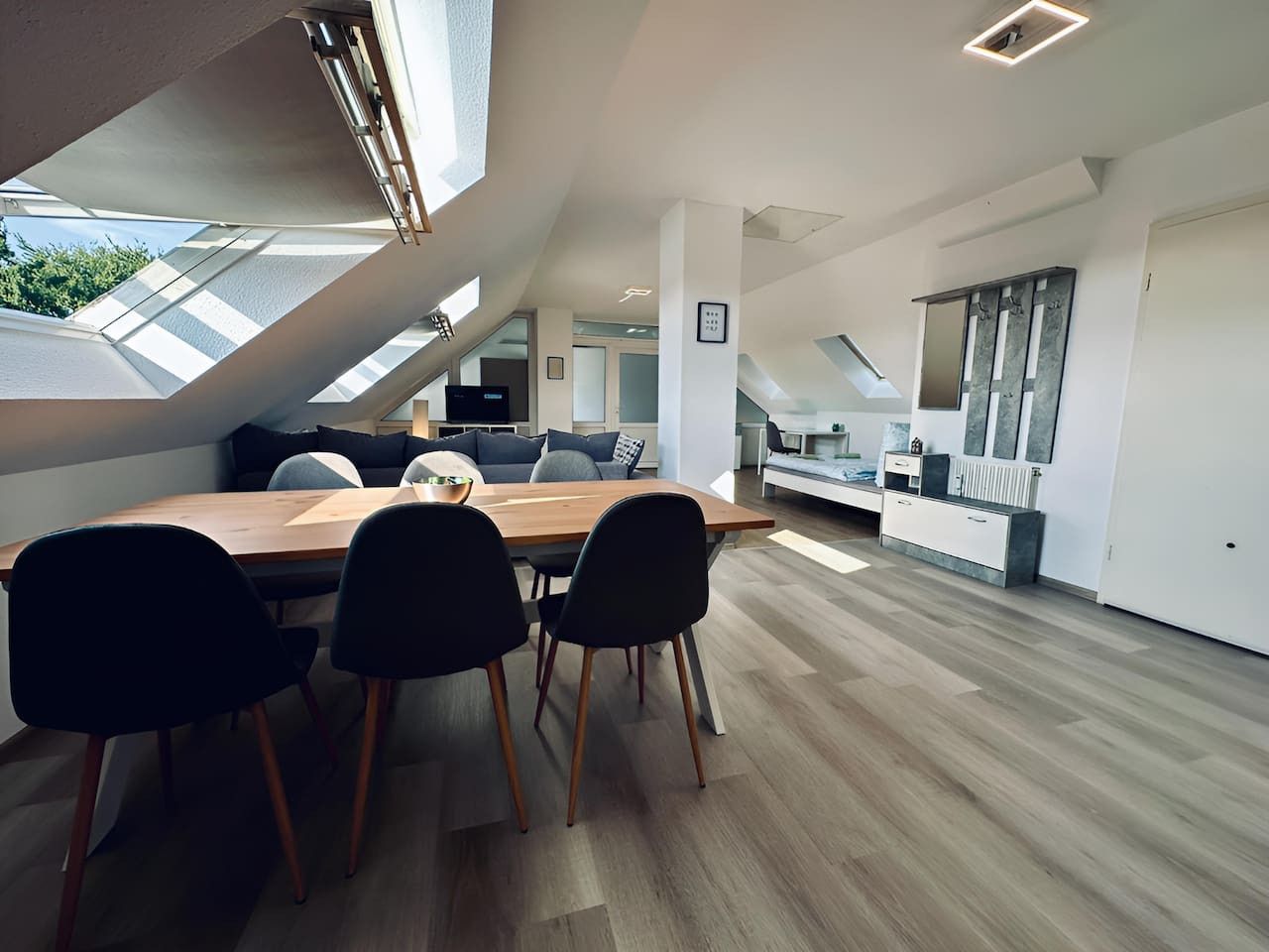 Ein modernes Interieur mit Essbereich, der einen Holztisch und schwarze Stühle umfasst, einer Küche mit weißen Schränken und einem Oberlicht, das für natürliches Licht sorgt.