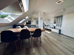 Een modern interieur met een eethoek bestaande uit een houten tafel en zwarte stoelen, een keuken met witte kasten, en een dakraam voor natuurlijk licht.