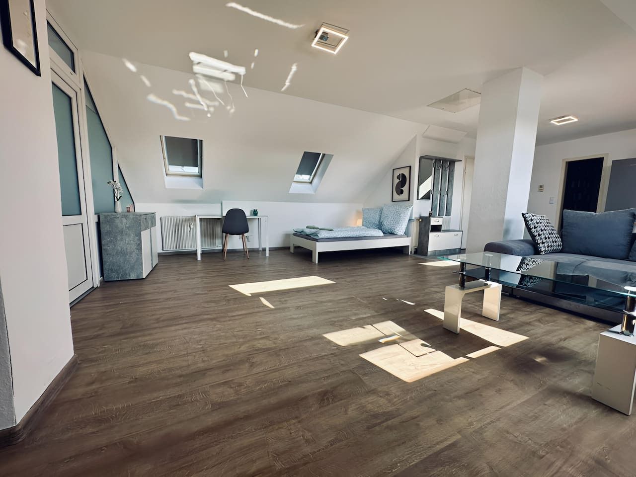 Amplio apartamento estilo loft con techo alto, tragaluces, cocina moderna, comedor y sala de estar con una mesa de centro de vidrio.