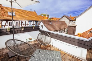 A rooftop terrace with a table, two chairs, and a patterned rug.