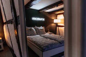 Ein Schlafzimmer mit Bett, Kissen, einer Nachttischlampe und einem Neonleuchtschild an der Wand.