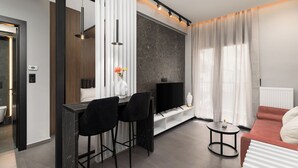 Uma sala de estar moderna com TV, dois taboretes pretos, uma mesa de centro redonda e um sofá vermelho.