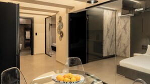 Ett modernt hotellrum med ett matbord i glas, en säng med en vit madrass och en vägg i marmor.