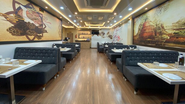 Um restaurante com assentos estofados em preto, piso de madeira e obras de arte nas paredes.