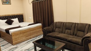 Quarto de hotel com cama, sofá marrom, mesa de centro com tampo de vidro e chão com padrão marmorizado.