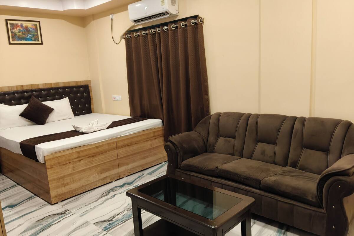 Una habitación de hotel con una cama, un sofá marrón, una mesa de centro de vidrio y un piso con diseño de mármol.