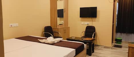A hotel room with a bed, two chairs, a desk, a flat-screen TV, an air conditioning unit, and a mirror.