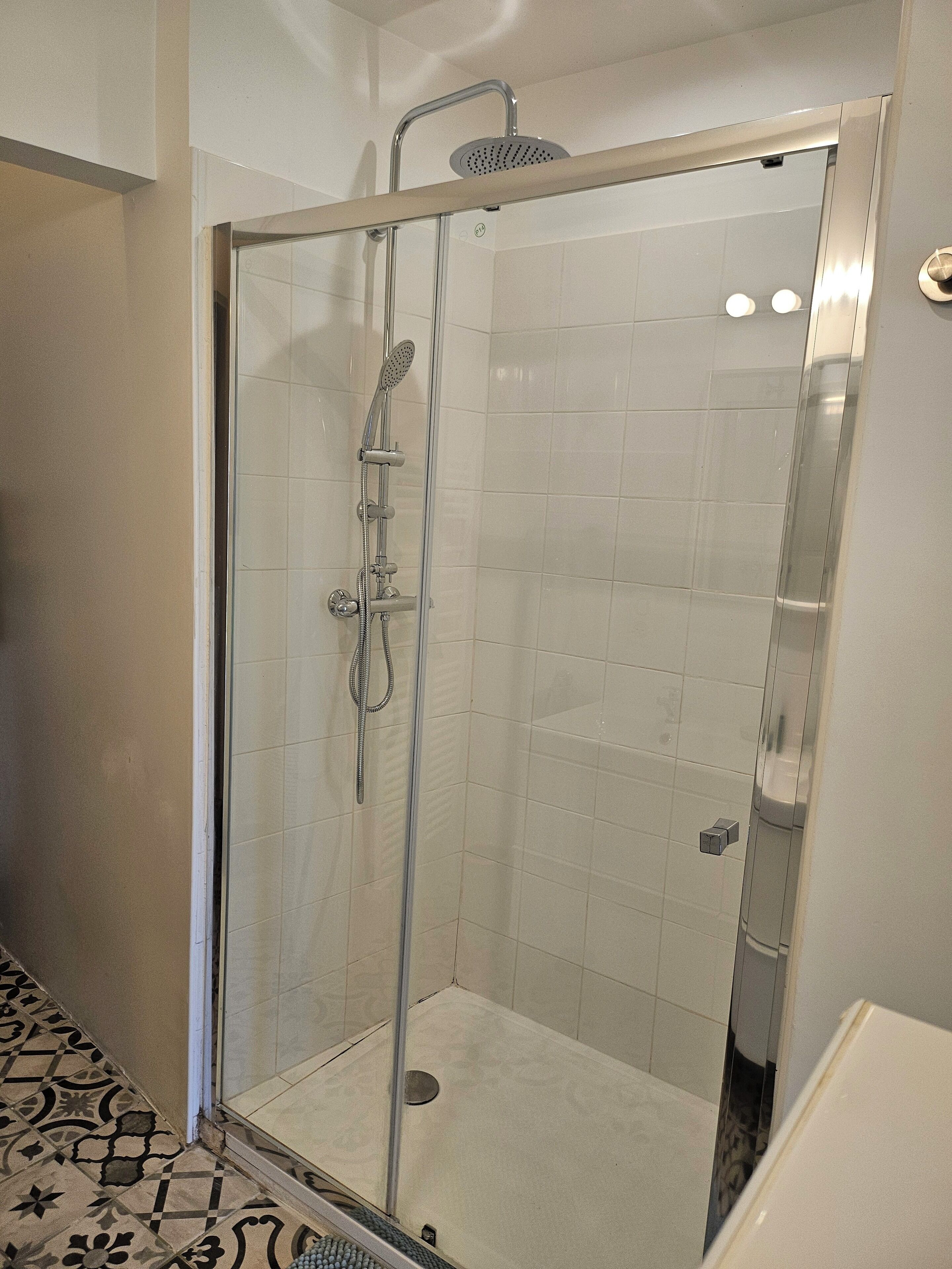A glass-enclosed shower with a handheld showerhead and a wall-mounted faucet.