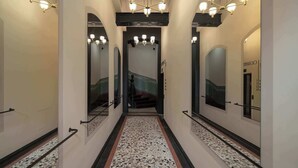 Un couloir doté d’un sol en terrazzo, de murs recouverts de miroirs et d’un lustre central.