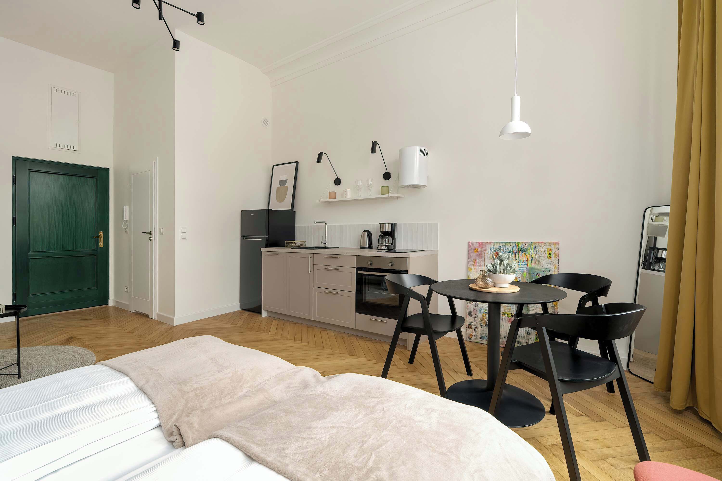A modern room with a bed, a desk, a chair, a small table, and a kitchenette.