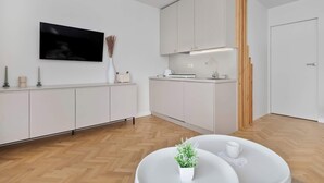 Una cocina moderna con armarios blancos, un televisor de pantalla plana sobre la encimera y una pared de acento de madera.