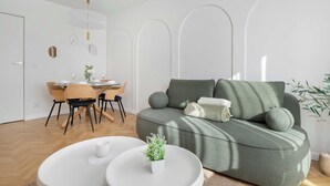 Una sala de estar moderna con un sofá verde, una mesa de comedor con sillas y una pequeña mesa blanca con una planta.