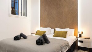 A modern hotel room with a large bed, a wooden accent wall, a bedside table with a lamp, and a window with a view. - Luxury Apt! 4BD/4BTH en suite (Madrid)