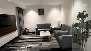 Una sala de estar moderna con un televisor de pantalla plana, un sofá gris, una mesa de centro y una planta grande en maceta.