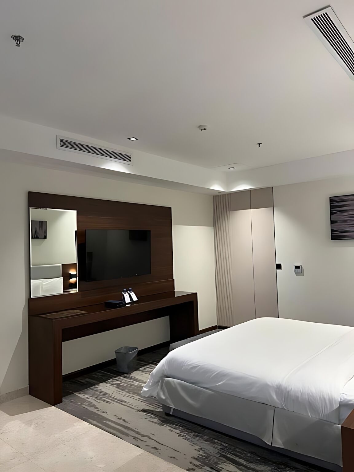 Un dormitorio de hotel moderno con una cama grande, televisión integrada, tocador con espejo y armario.