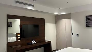 Un dormitorio de hotel moderno con una cama grande, televisión integrada, tocador con espejo y armario.