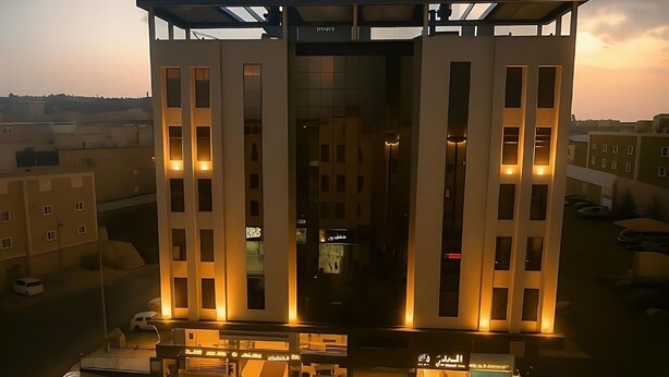 Un edificio moderno con fachada de vidrio, varios balcones e iluminación de letreros.