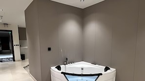Un baño moderno con una bañera independiente, zona de ducha y una cocina visible al fondo.