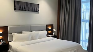 Una habitación de hotel moderna con una cama grande, cabecero, lámparas de noche, una obra de arte en la pared y una ventana con cortinas.