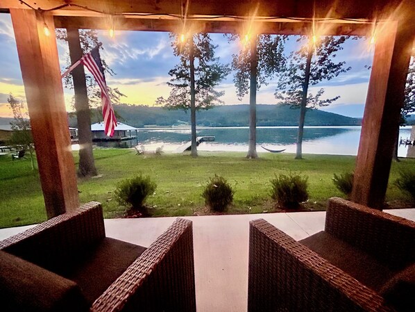An outdoor seating area with wicker furniture, overlooking a lake with trees and a distant mountain range. - Lakefront w/ Private Dock + Sunset Views | Sleeps 8 | Near Boat Launch (Grant)