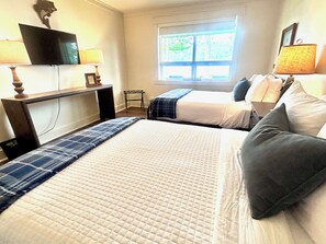 A hotel room with two beds, a desk with a lamp, a TV, and a window with a view of greenery. - Lakefront w/ Private Dock + Sunset Views | Sleeps 8 | Near Boat Launch (Grant)