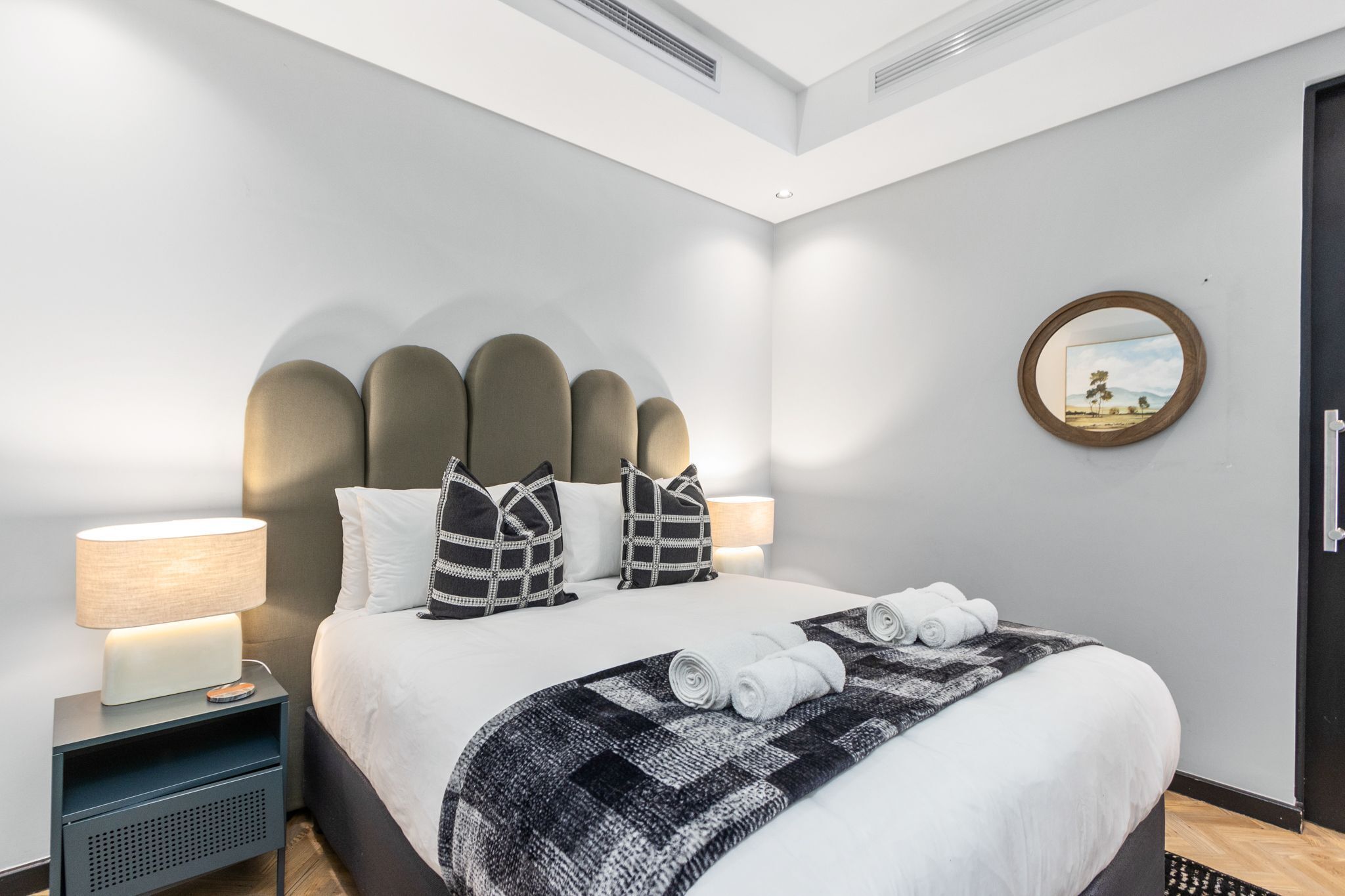 Ett modernt hotellrum med en stor säng, två sänglampor, en rund spegel och utsikt över omgivningarna genom fönstret.