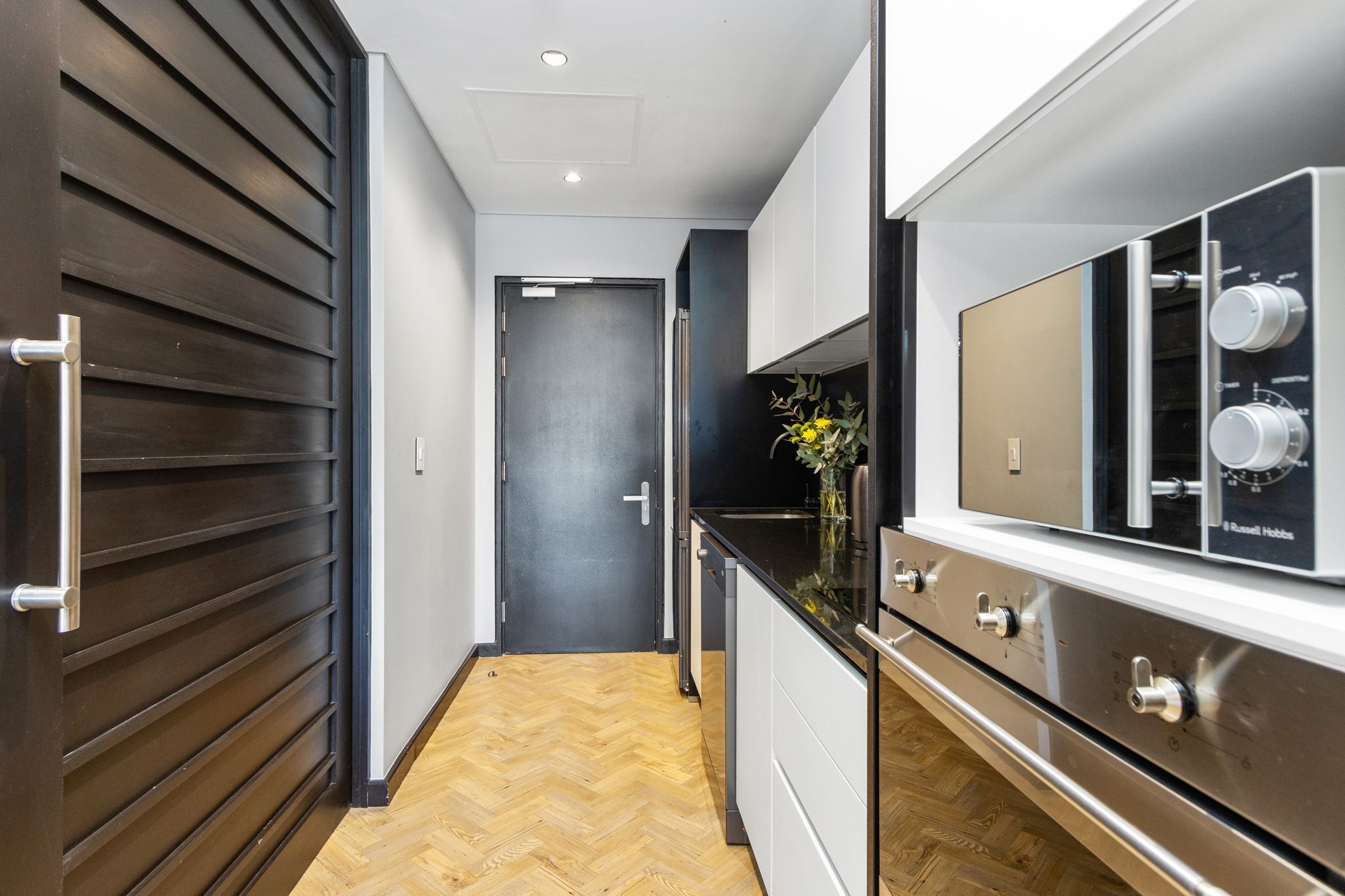A modern kitchen with a stainless steel range hood, wooden flooring, and a dark door.