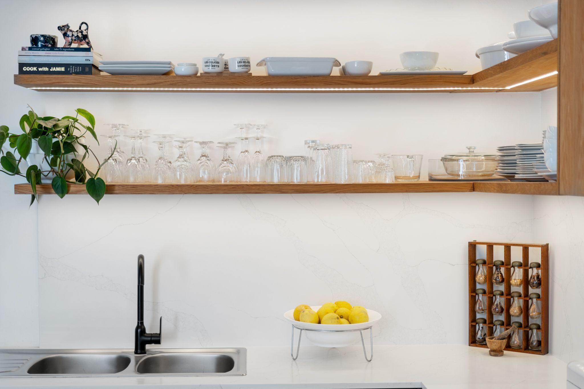 A kitchen with a wooden shelf holding glassware and a bowl of lemons.